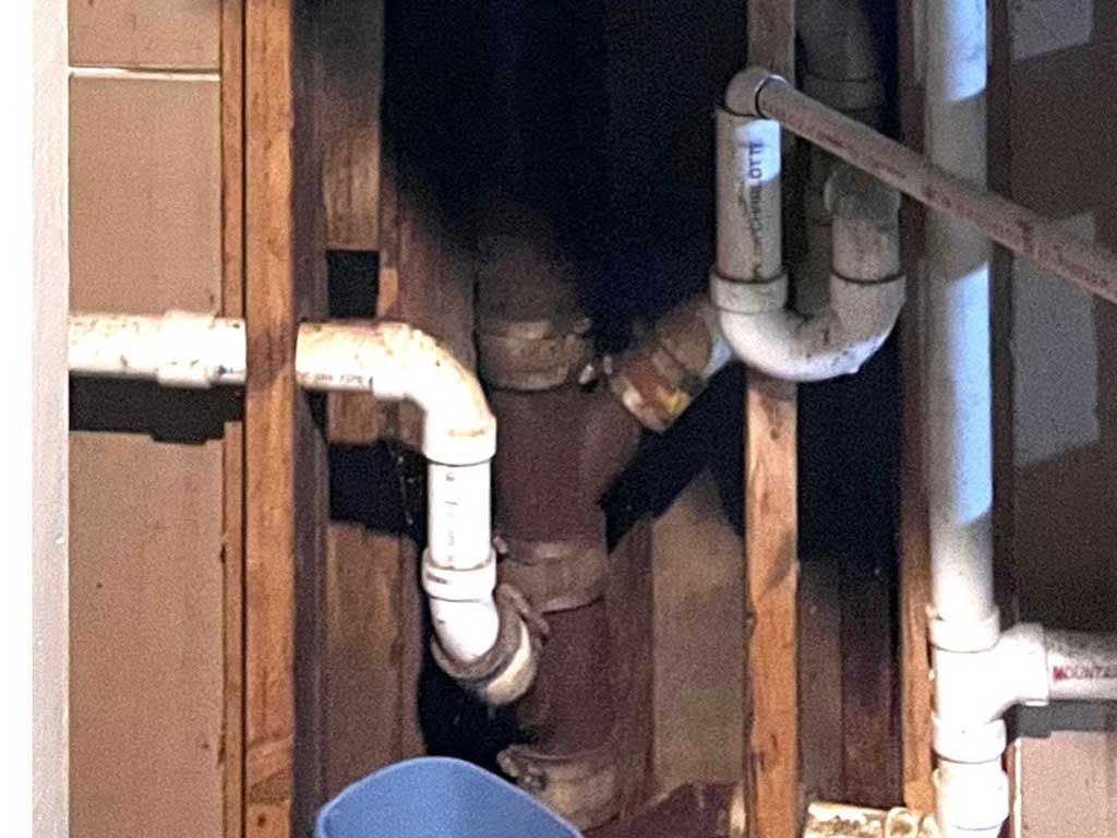 Exposed white plumbing pipes and wooden framing inside an unfinished wall.
