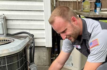 Technician inspecting an air conditioner unit outside a house