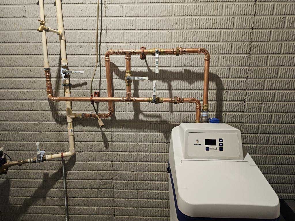 Wall-mounted plumbing and pipes above a white water softener in a utility room