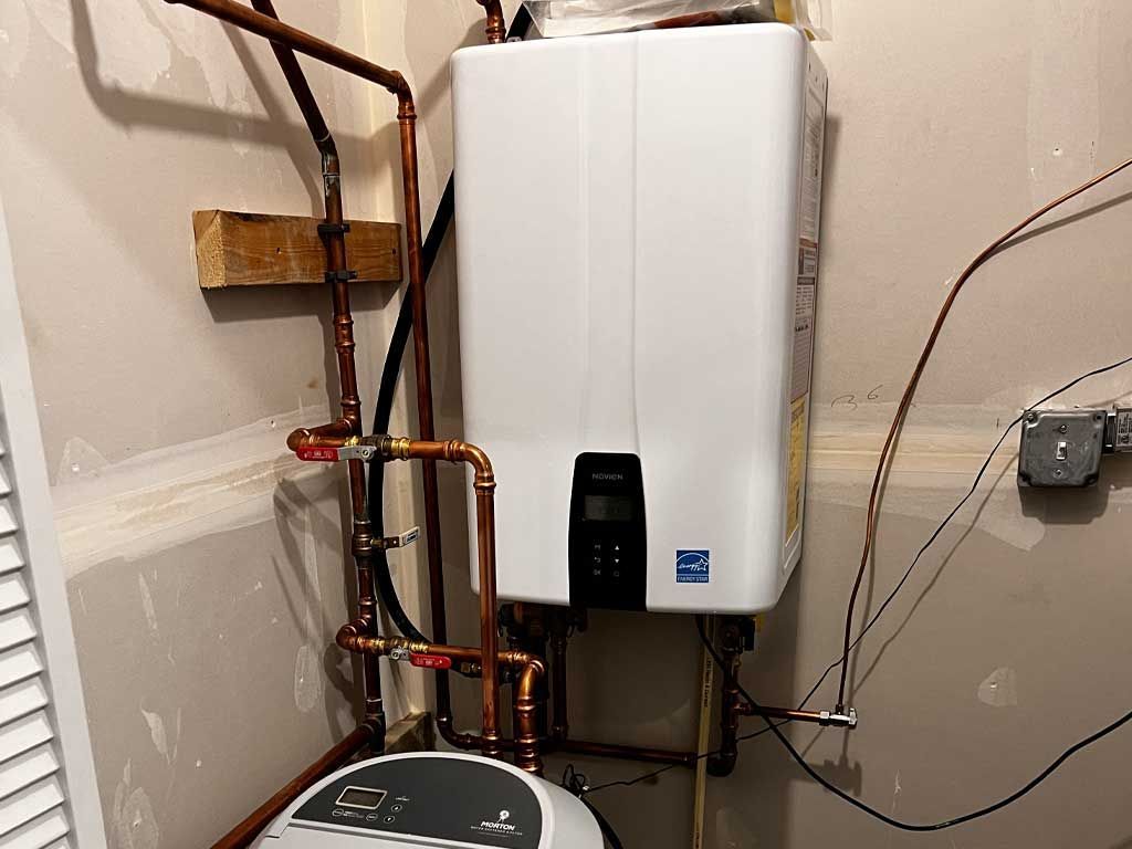 Wall-mounted white water heater with copper pipes in a utility closet or basement room.