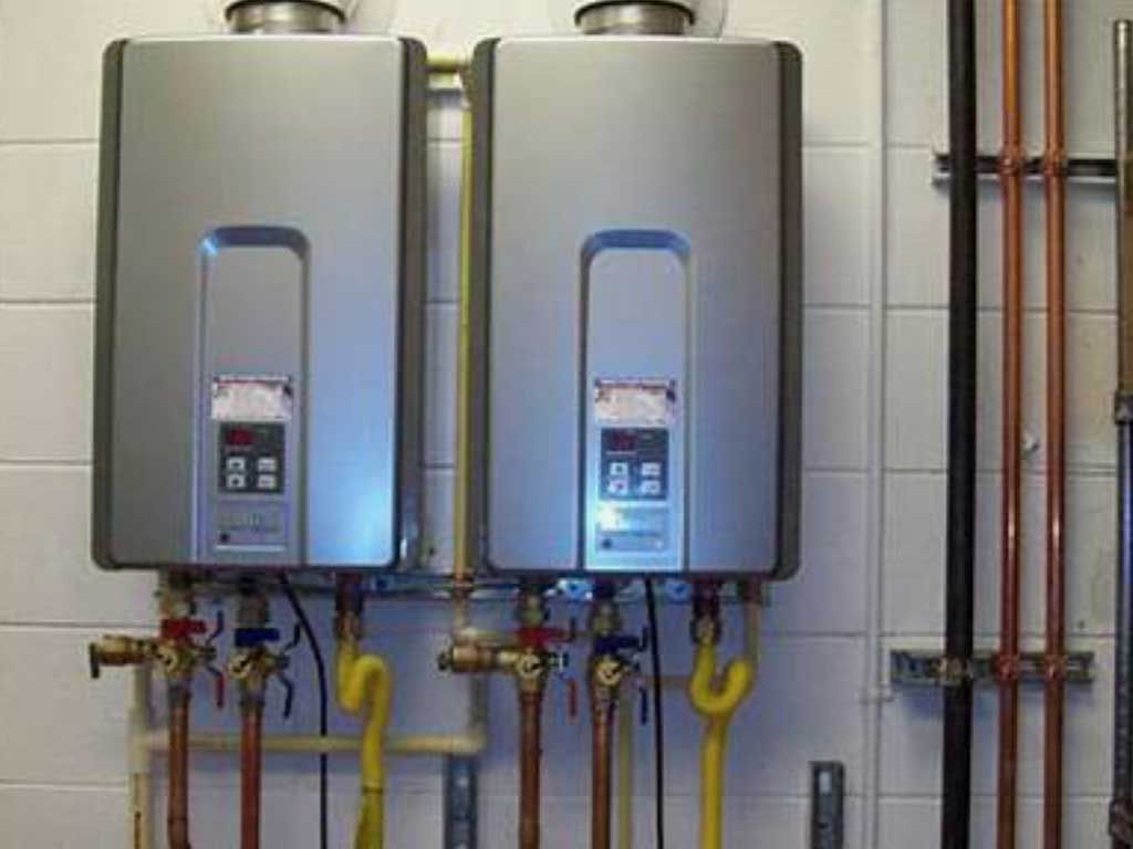 Two wall-mounted silver water heaters with yellow gas lines and copper pipes in a tiled utility room
