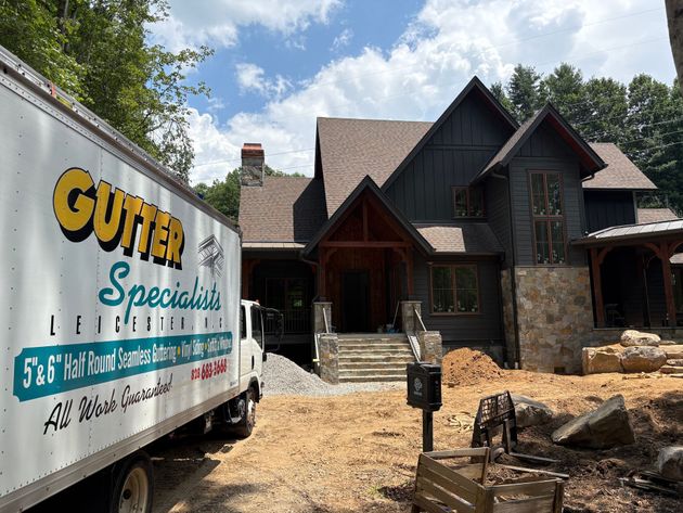 Gutter specialist truck parked in front of a house. The house is brown and black, under construction.