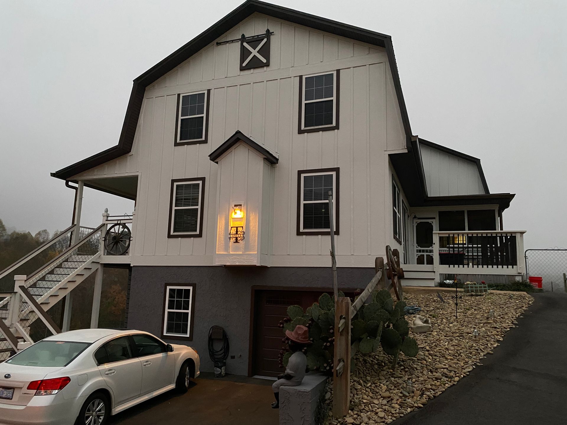 White barn-style house with gray base, porch, and a white car parked in front. Overcast day.