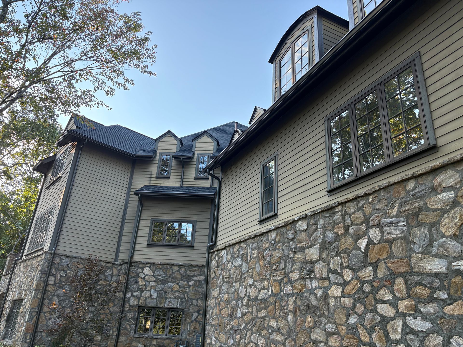 Stone and wood-sided building with multiple stories and windows. Dark gray roof and blue sky visible.