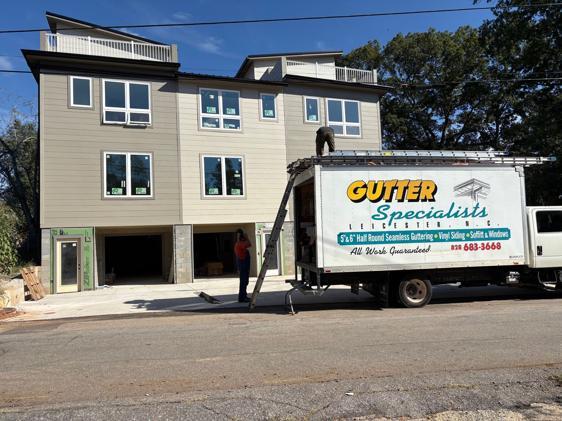 Gutter specialists working on a multi-story building. A truck with a ladder is parked in front.