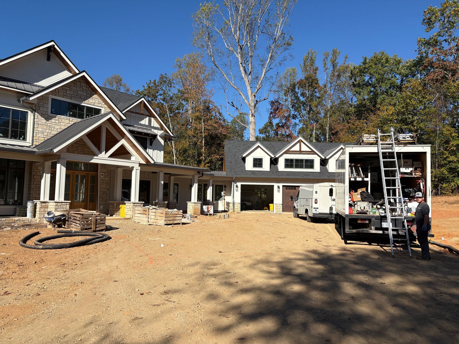 Two-story house under construction with a construction truck. Dirt ground. Clear, sunny day.