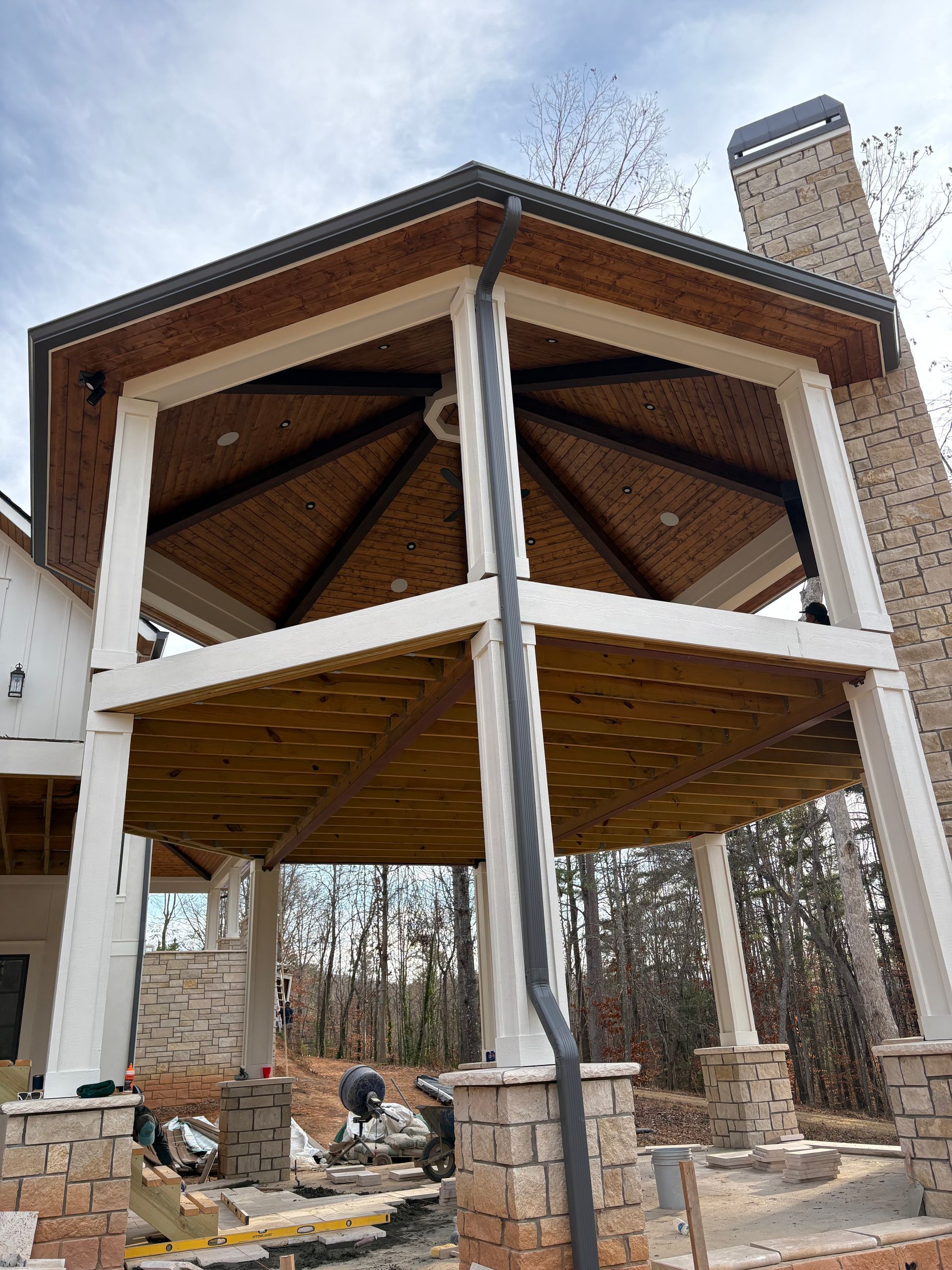 Outdoor pavilion under construction with brick pillars, white posts, and a wood ceiling.