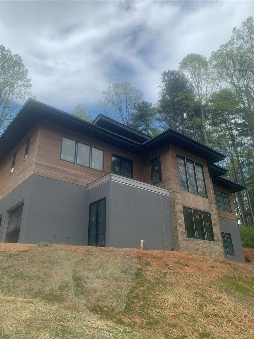 Modern brick house with gray siding, large windows, and dark roof, on a hillside with trees.