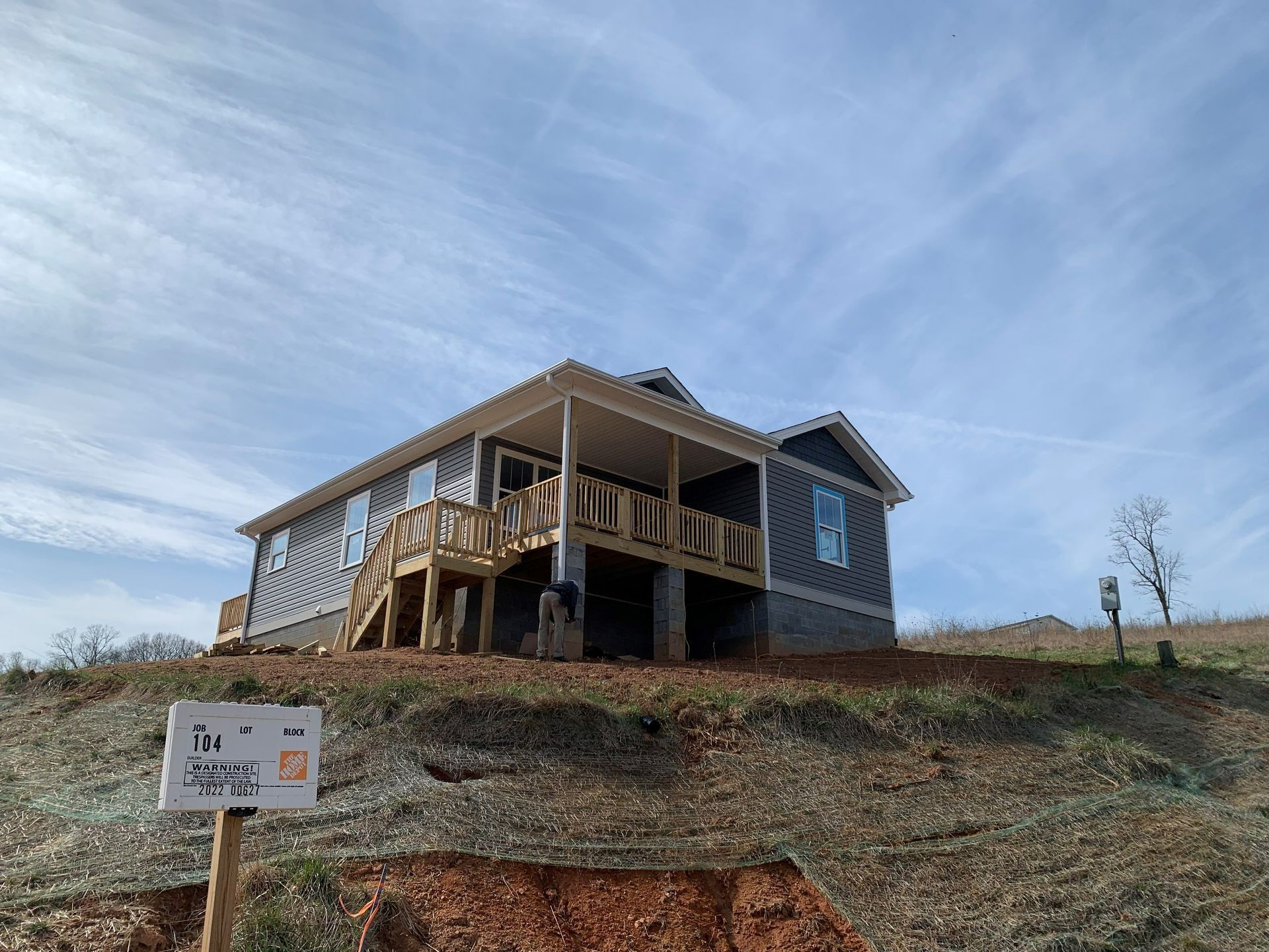 New house under construction on a hillside, with a wooden porch and siding. Blue sky.