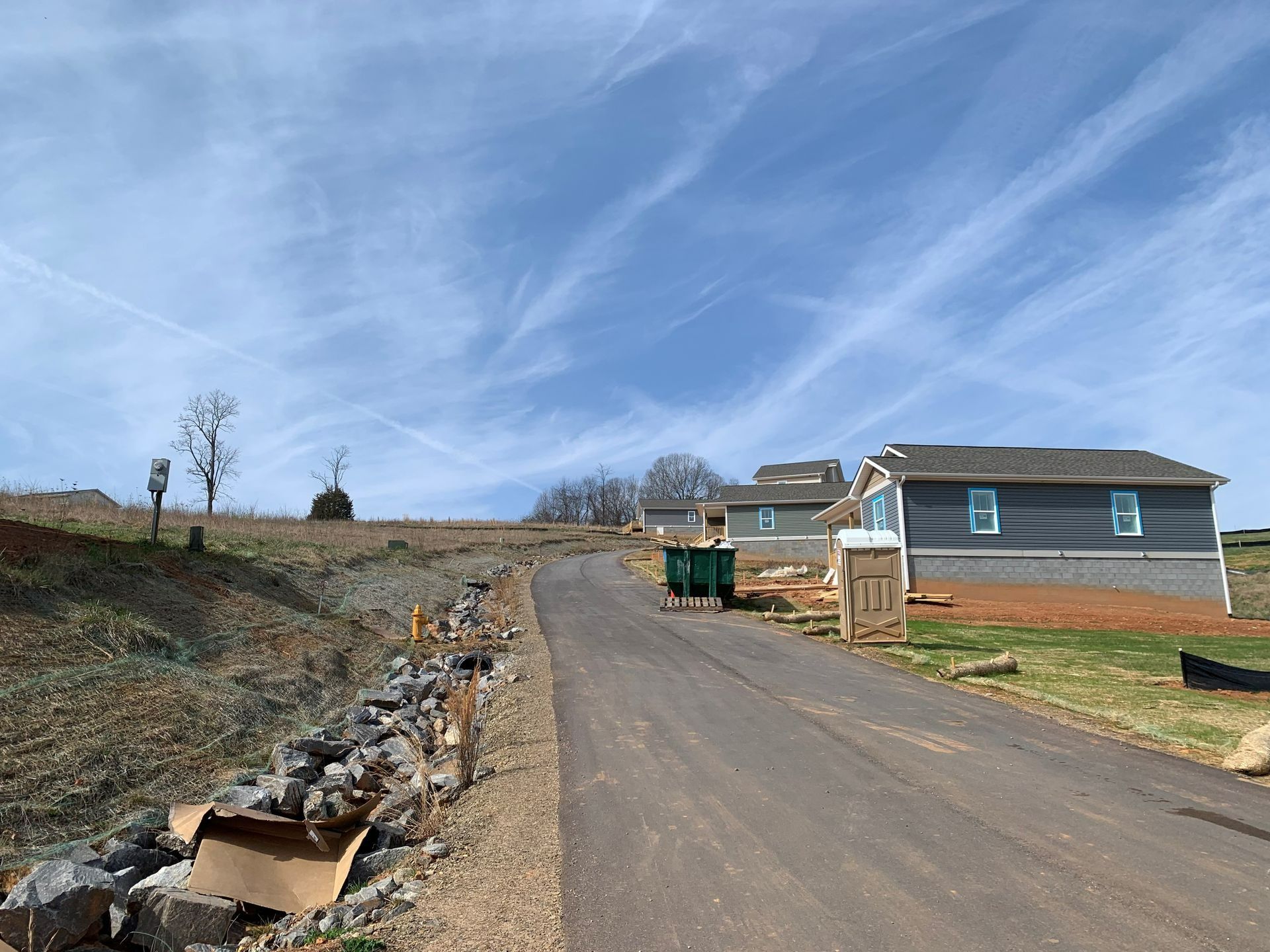 Paved road leading uphill past new construction homes. Blue sky with clouds.