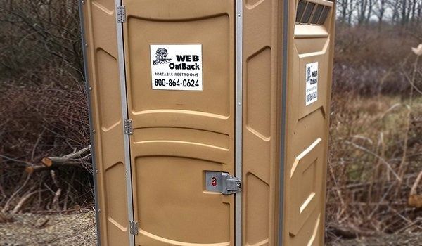 A brown portable toilet is sitting in the middle of a field.