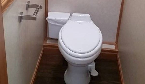 A white toilet is sitting in a bathroom next to a trash can.