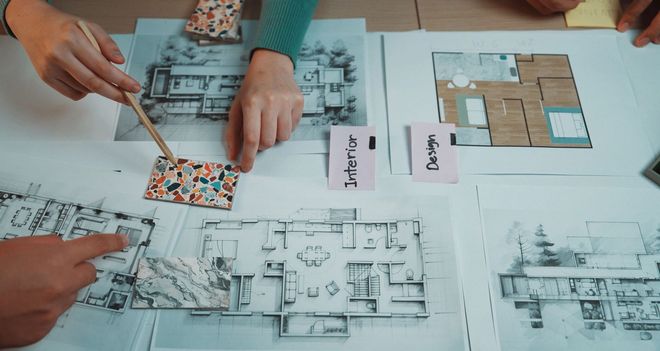 Hands pointing at blueprints, swatches, and sticky notes labeled
