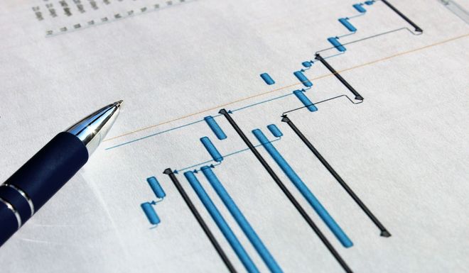Pen resting on a Gantt chart, a blue and white project schedule used for planning and tracking tasks.