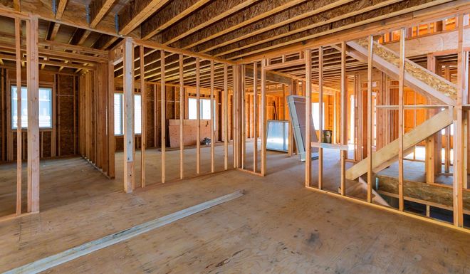 Interior of a house under construction; wood framing of walls, floors, and stairs.