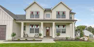 A white farmhouse with a porch, adorned with Christmas wreaths, in a sunny, residential setting.