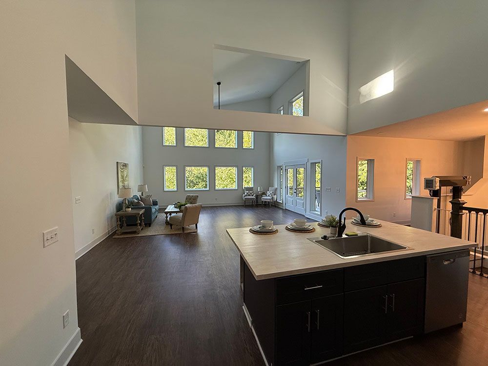Spacious, open-concept living space with dark cabinets, an island, high ceilings, and large windows.