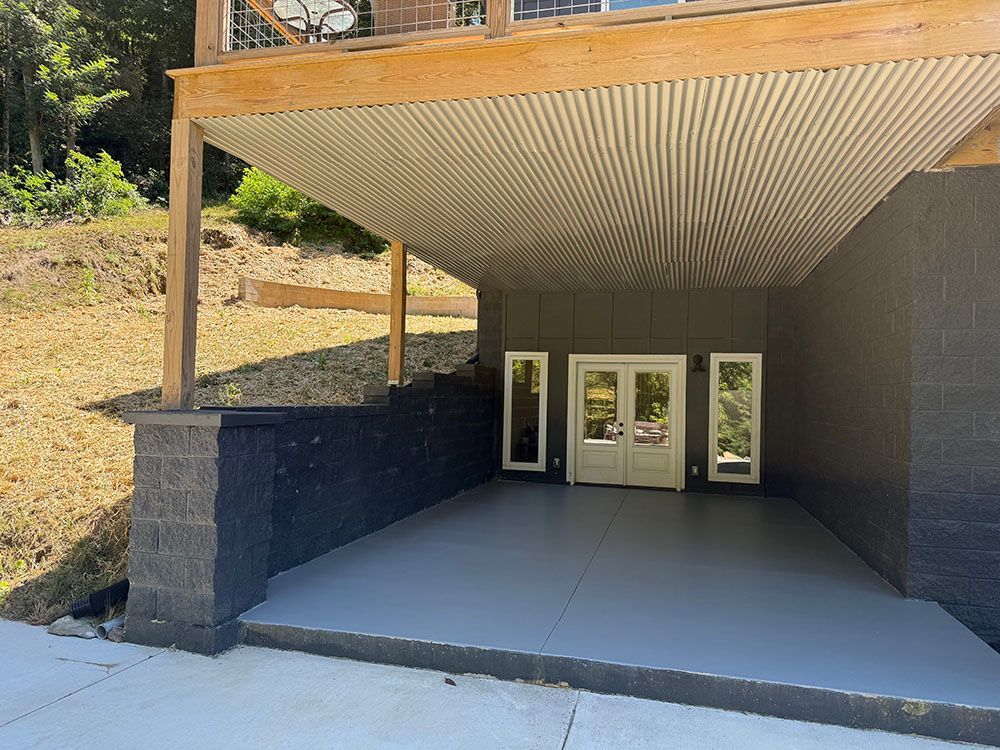 Gray covered carport entrance with French doors, a gray concrete floor and a retaining wall.