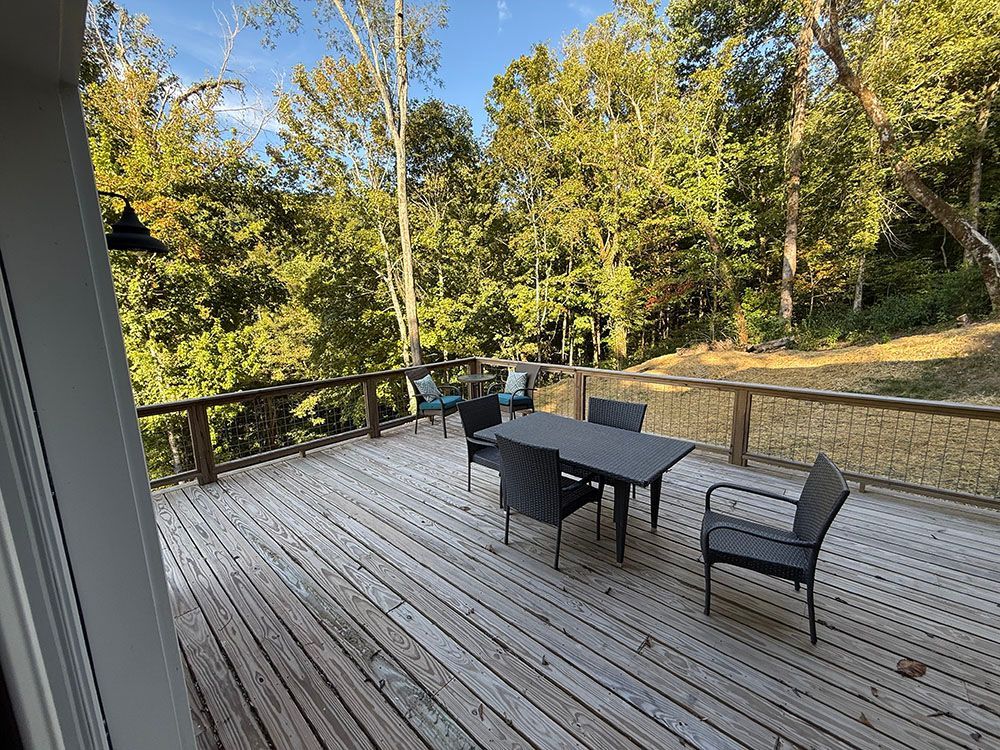 Wooden deck with table, chairs, and view of trees.