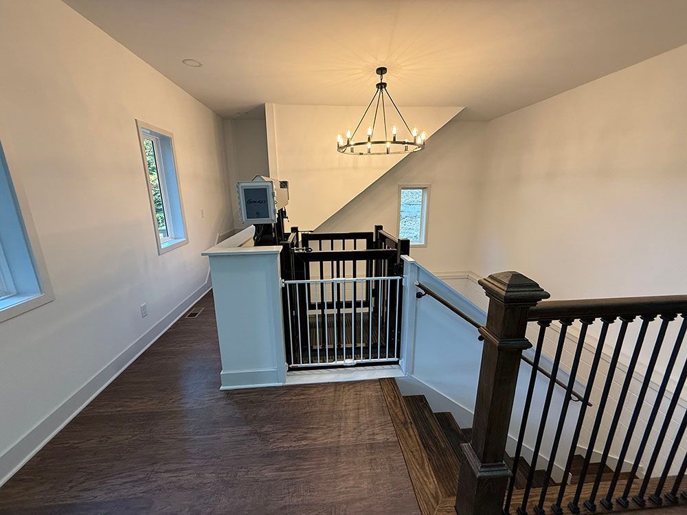 Interior with stair lift and stairs, dark wood floor, white walls, chandelier.