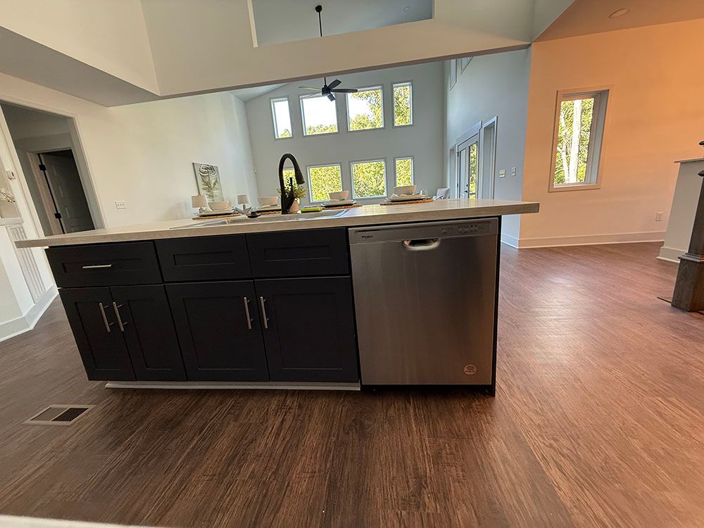 Kitchen island with black cabinets, stainless steel dishwasher, and gray countertop in a bright, open-concept space.