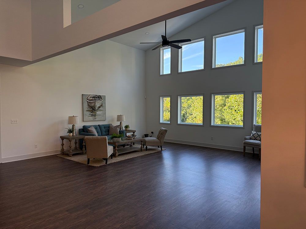 Spacious living room with high ceilings, tall windows, teal sofa, and wood flooring.