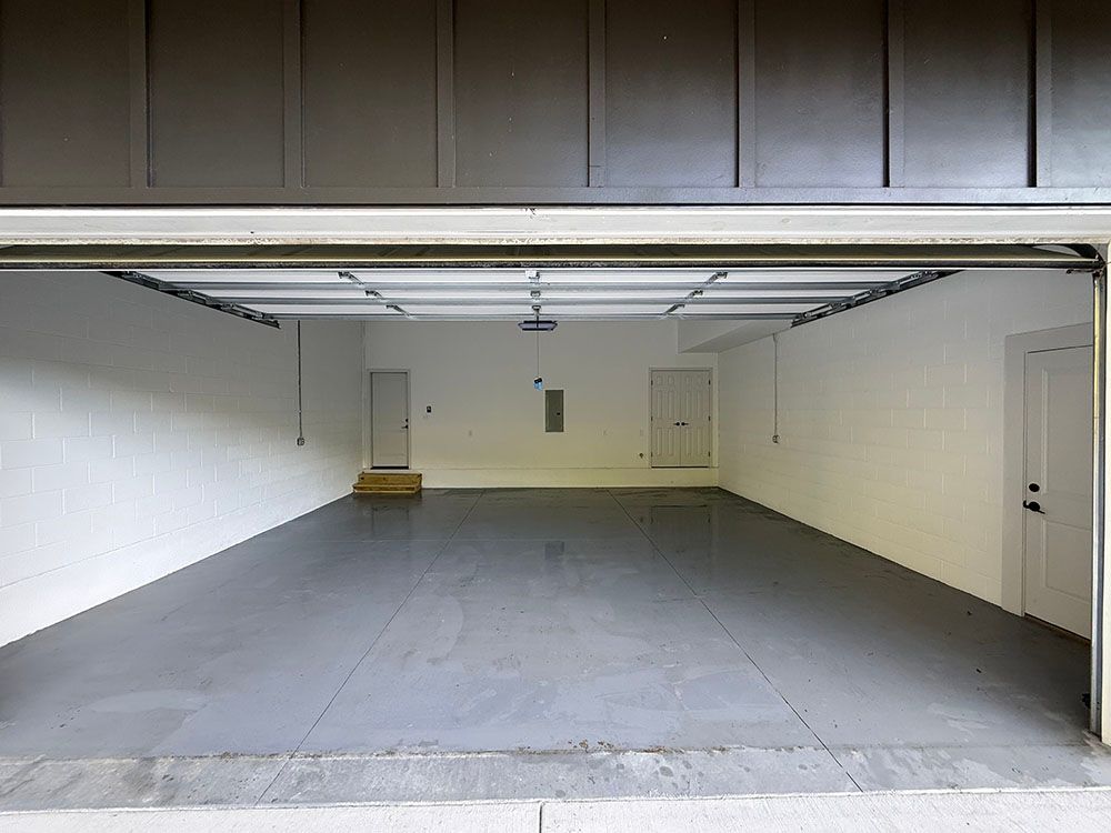 Empty, open garage with gray floor and white walls. Two doors and overhead garage door rails are visible.