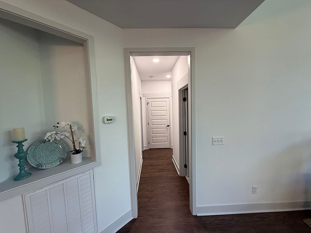 Hallway with white walls, dark wood floor, and recessed shelf with decor.