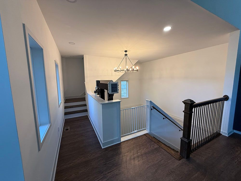Hallway with stairs and chandelier. Dark wood floor. White walls.