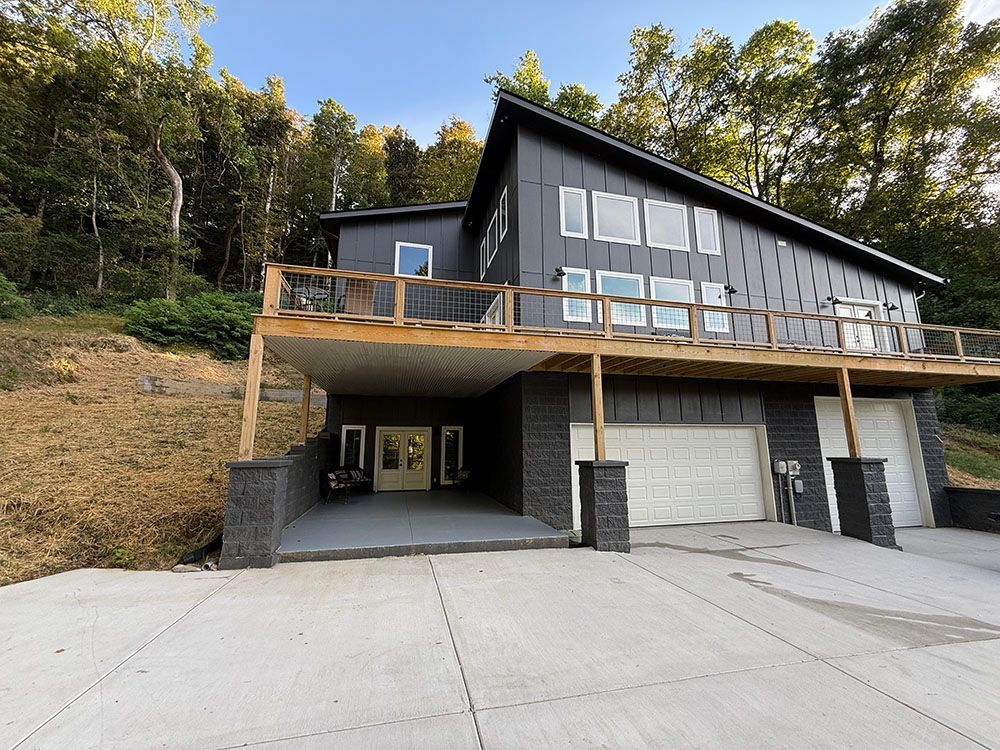 Modern gray house with a deck and a slanted roof, built into a hillside with a concrete driveway.