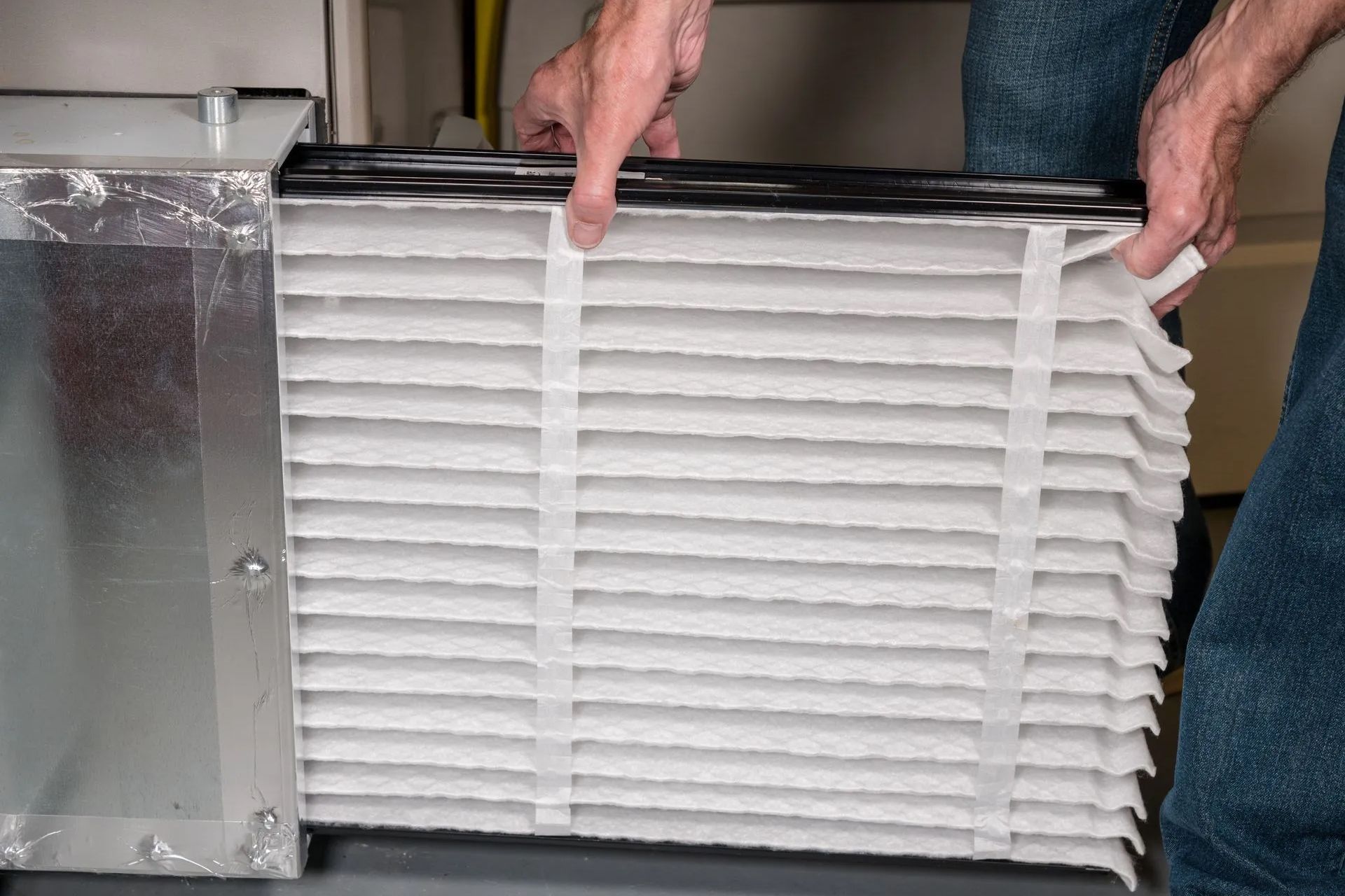Person replacing a pleated air filter in an HVAC unit.