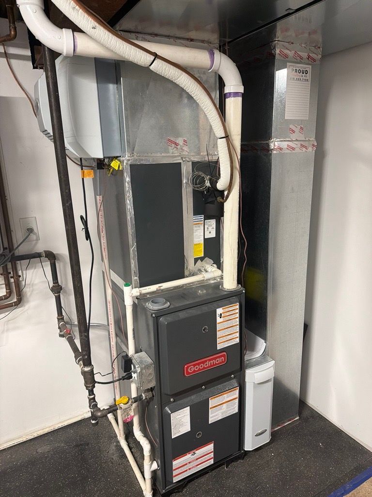 Furnace and water heater in a utility room. Gray and black metal appliances with white PVC pipes.