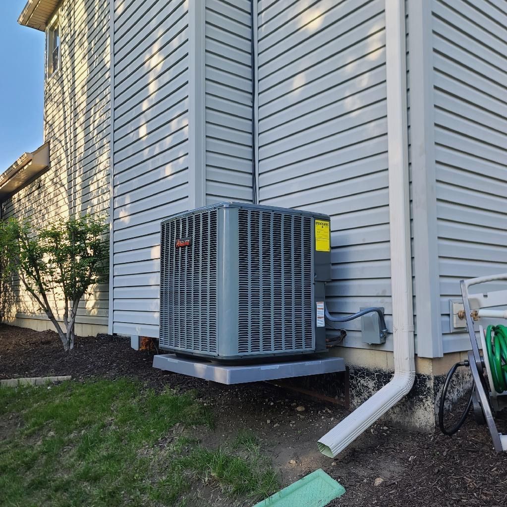 Air conditioning unit mounted on a concrete pad next to a house with gray siding.