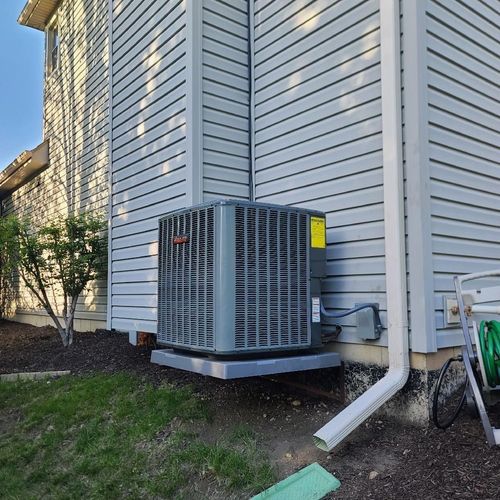Air conditioning unit mounted on a concrete pad next to a house with gray siding.