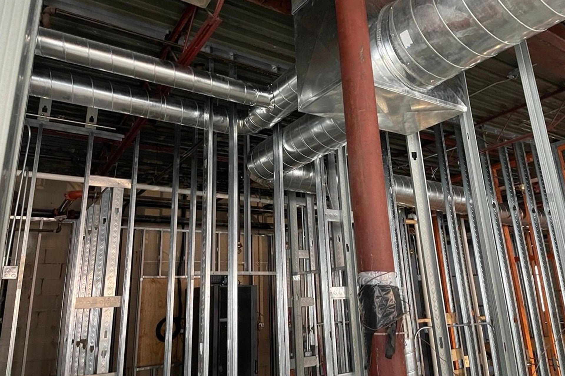 Construction site showing metal wall framing studs and silver HVAC ductwork suspended from the ceiling.