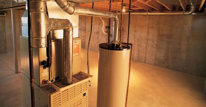 Furnace and water heater in a basement. Beige appliances with silver ductwork. Concrete walls and floor.