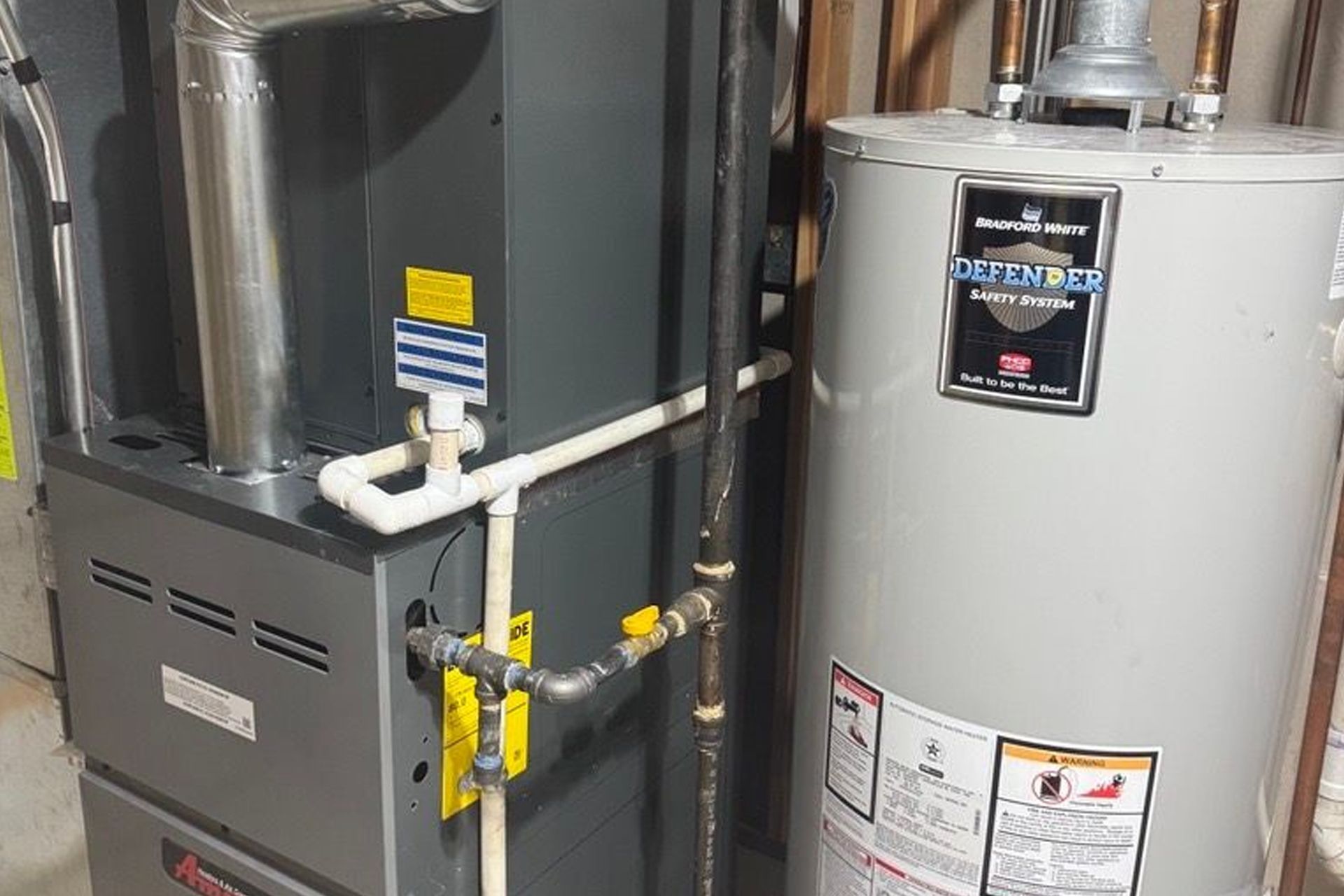 Furnace and water heater in a utility room. Gray appliances with connected pipes and vents.
