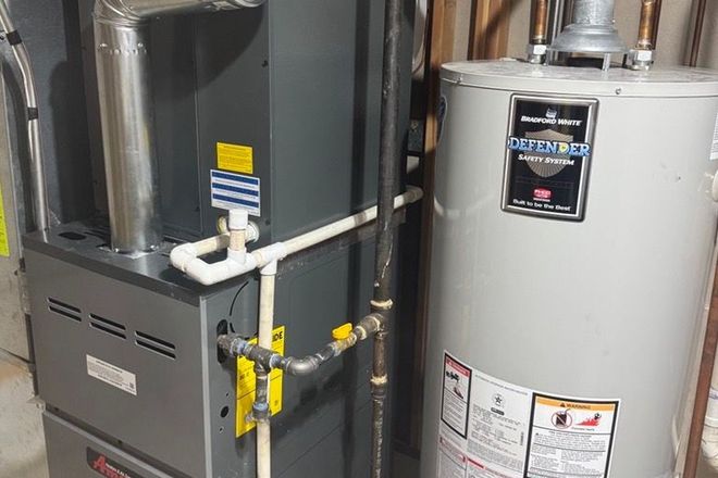 Furnace and water heater in a utility room. Gray appliances with connected pipes and vents.