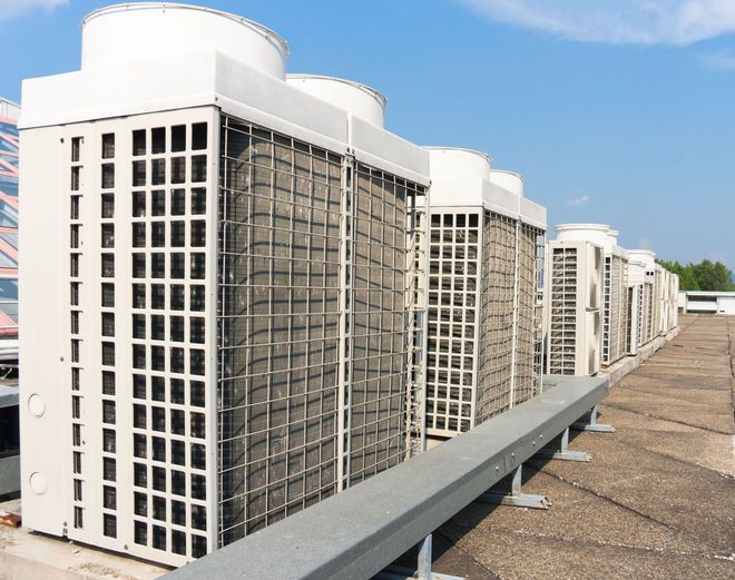 Rooftop air conditioning units lined up on a flat rooftop on a sunny day.