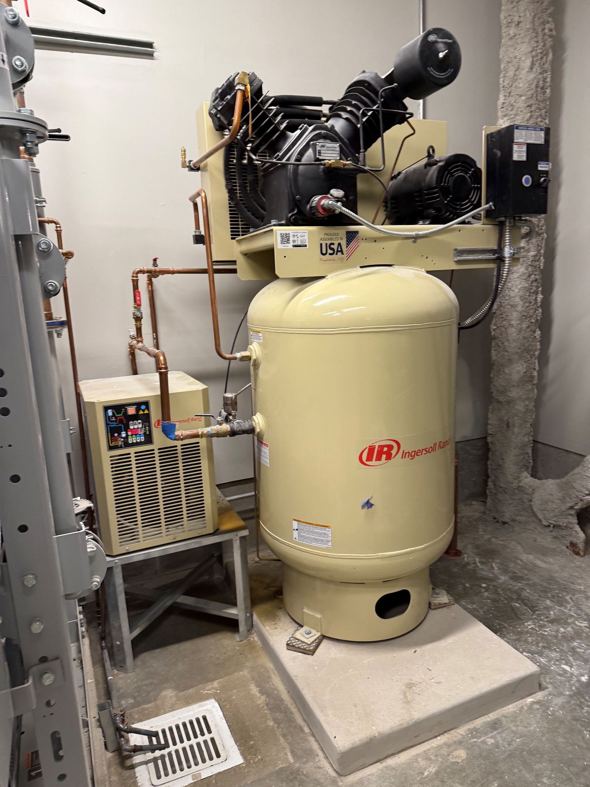 Air compressor with tank and chiller in a utility room. Beige and black machinery.