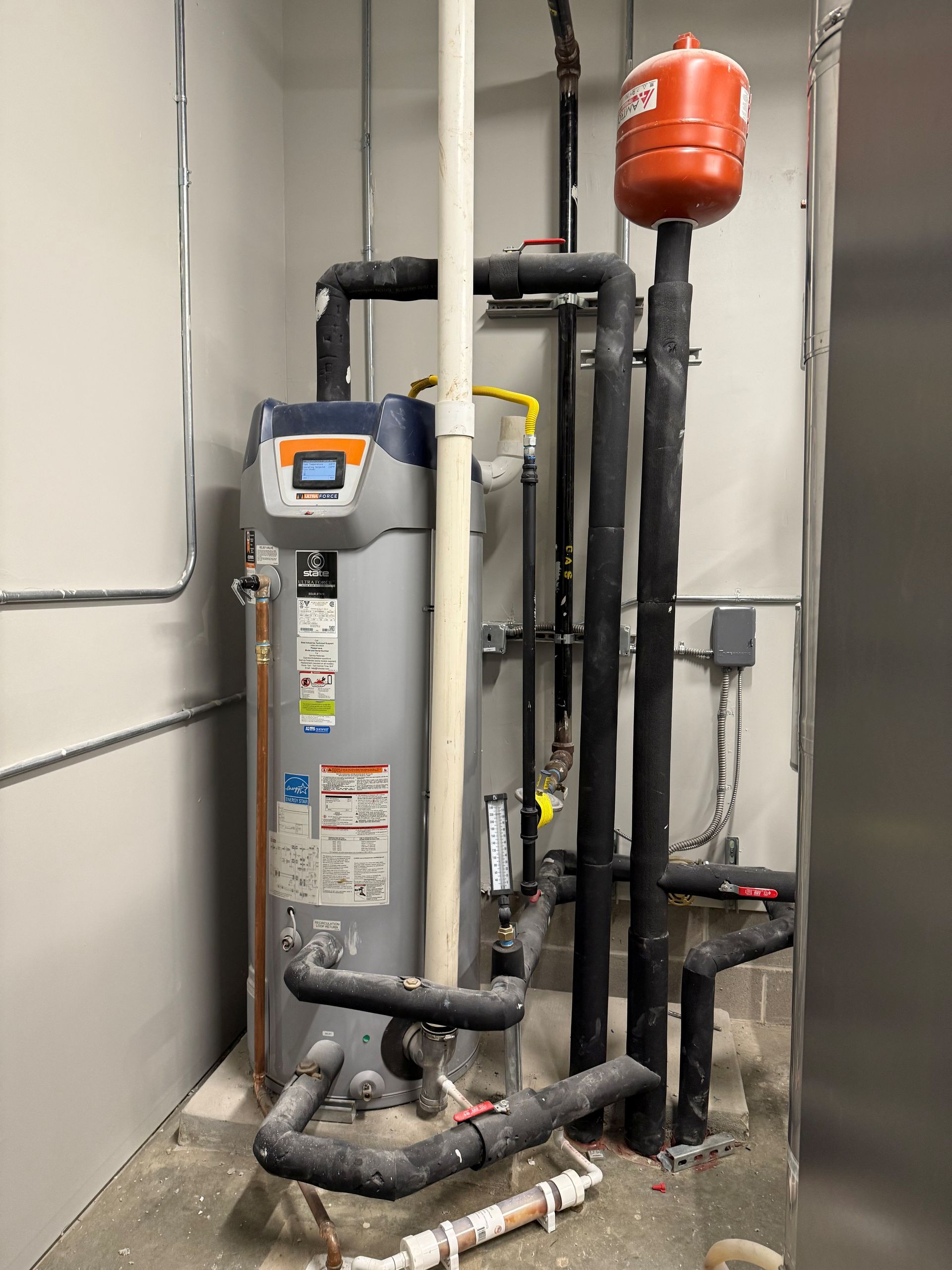 Water heater and associated pipes in a utility closet with a red expansion tank.