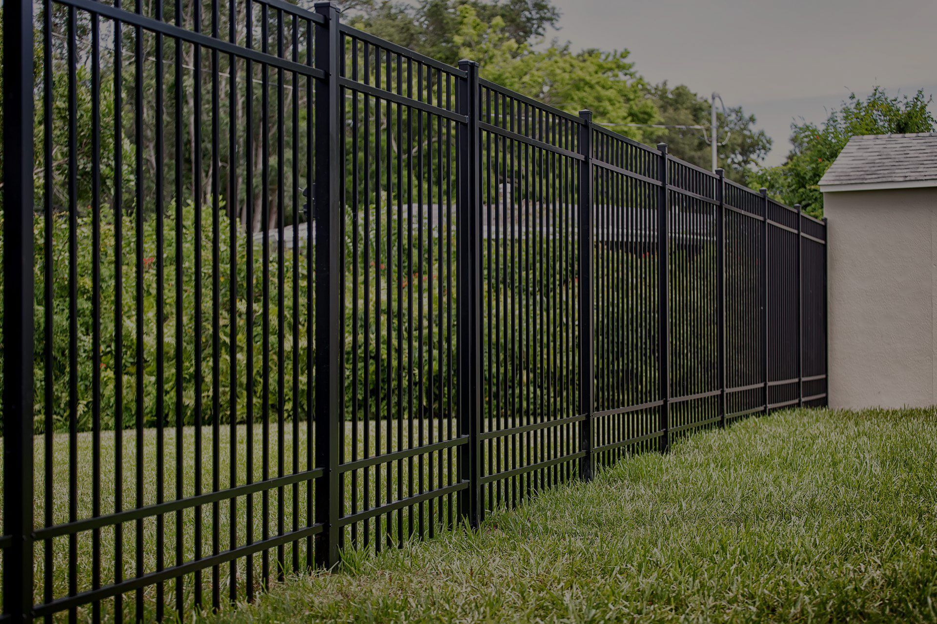 Black metal fence on a green lawn with trees in the background, next to a beige building.