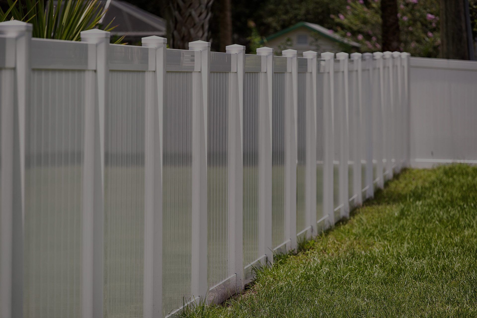 White vinyl privacy fence along a grassy lawn in a residential area.