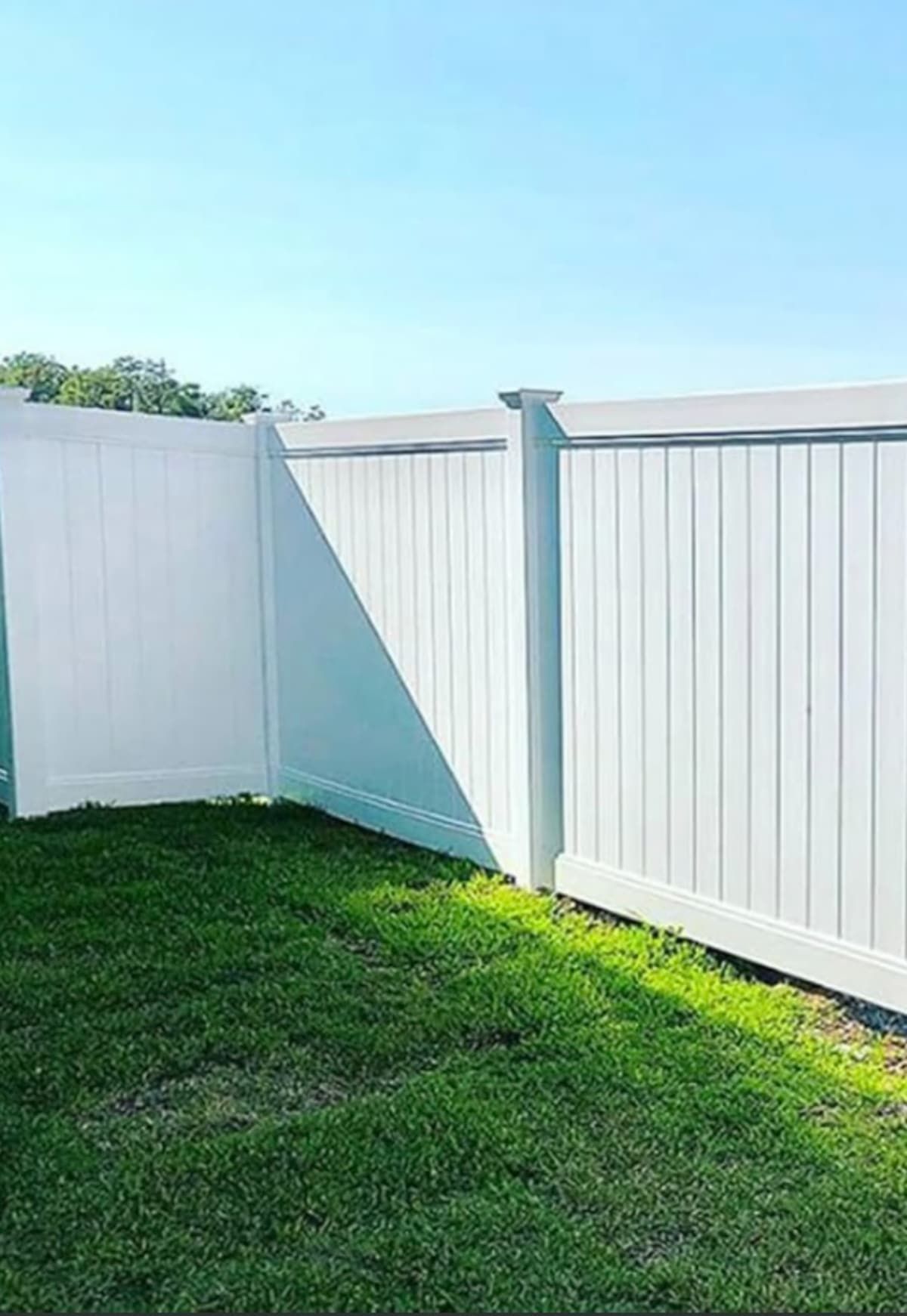White vinyl fence in a grassy yard under a blue sky. A section of the fence is angled.