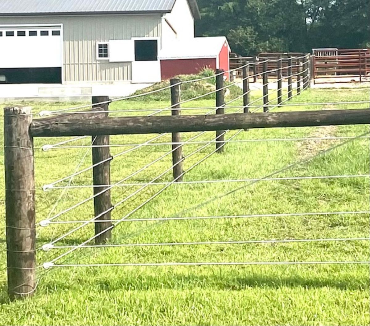 Wooden fence with wire strands in a grassy field, barn in the background.