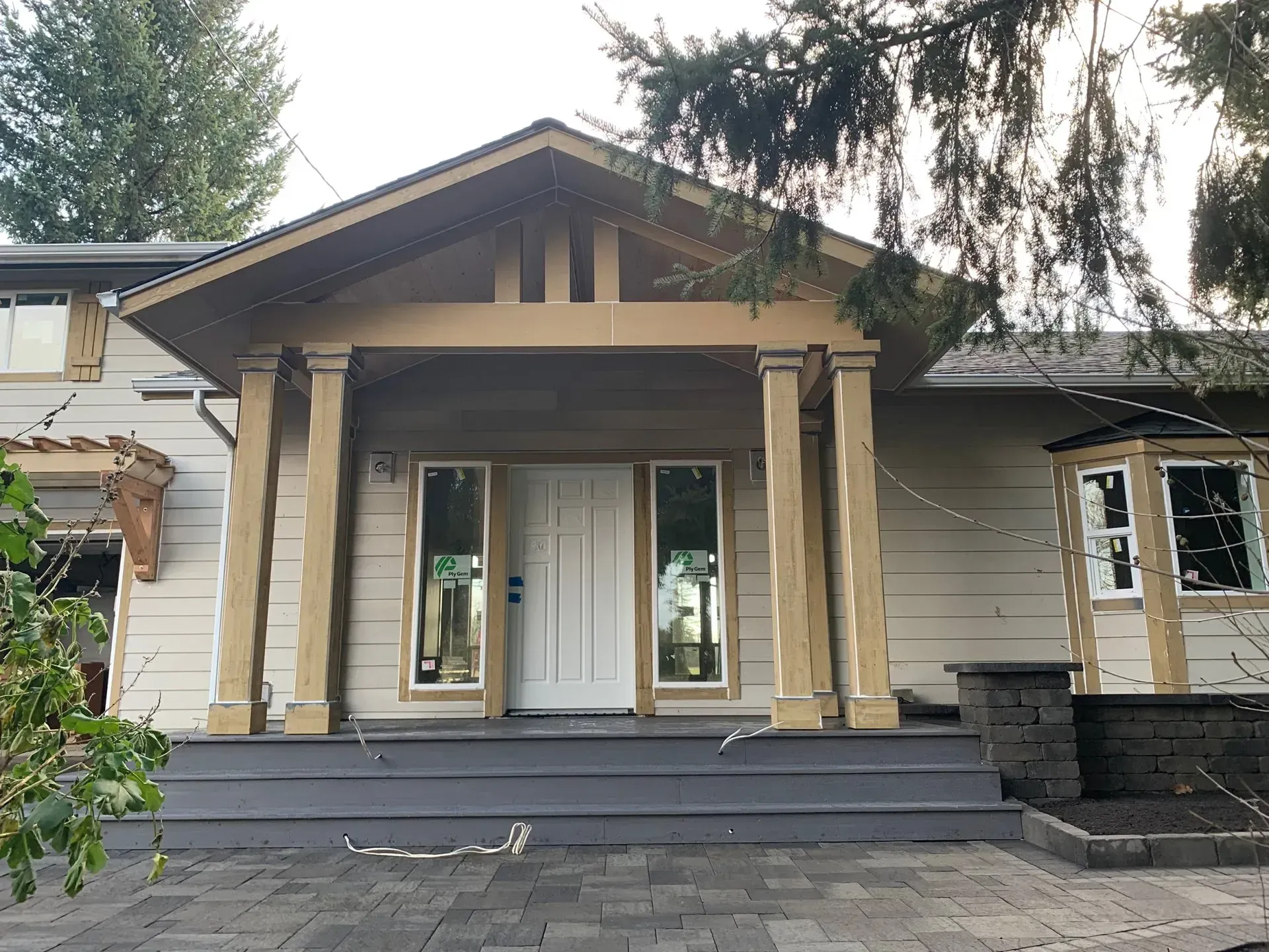 Front porch of a house with pillars, gray steps, and white door. Trees in the background.