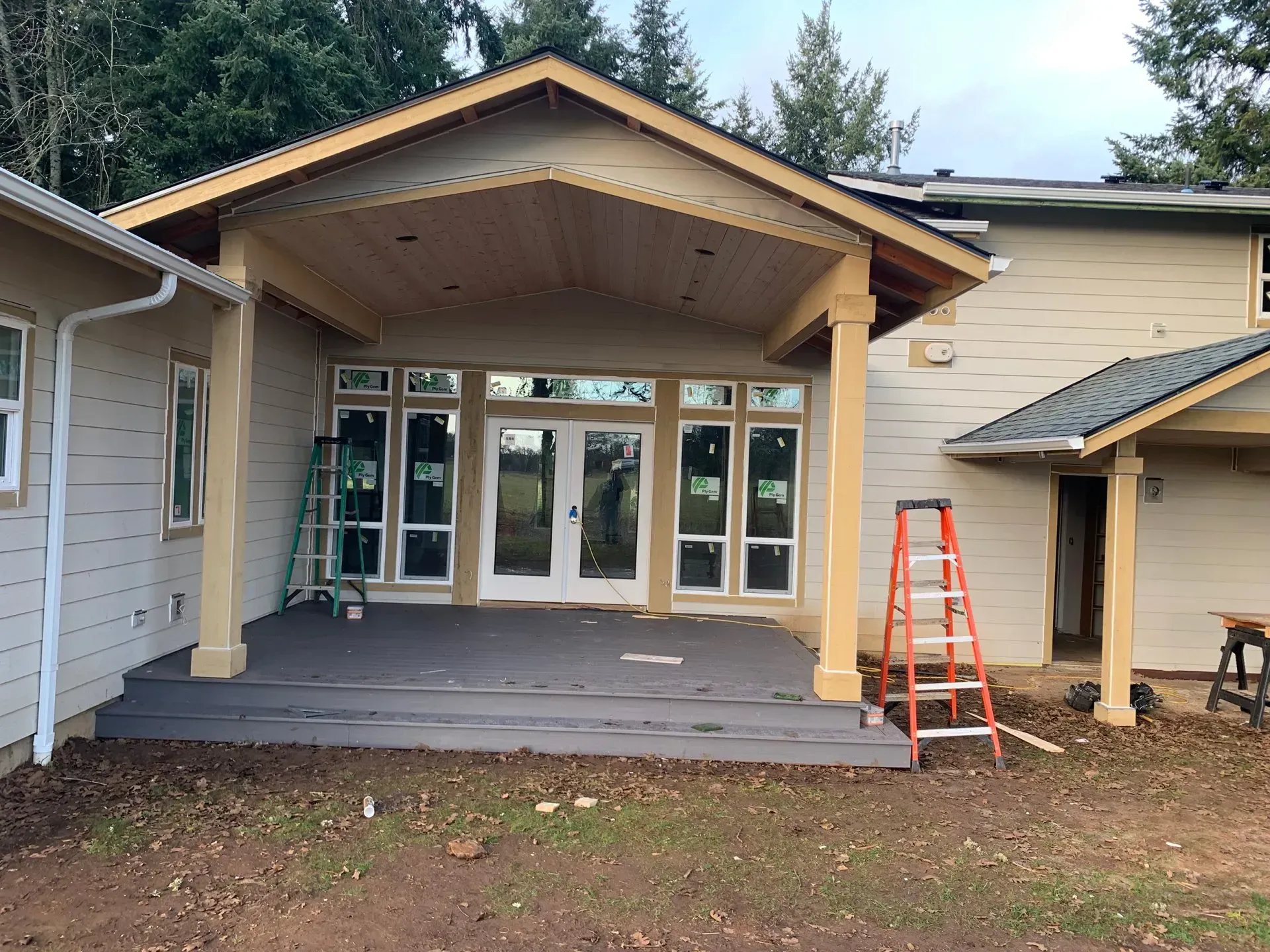 A covered porch with windows and double doors is under construction; a ladder stands nearby.