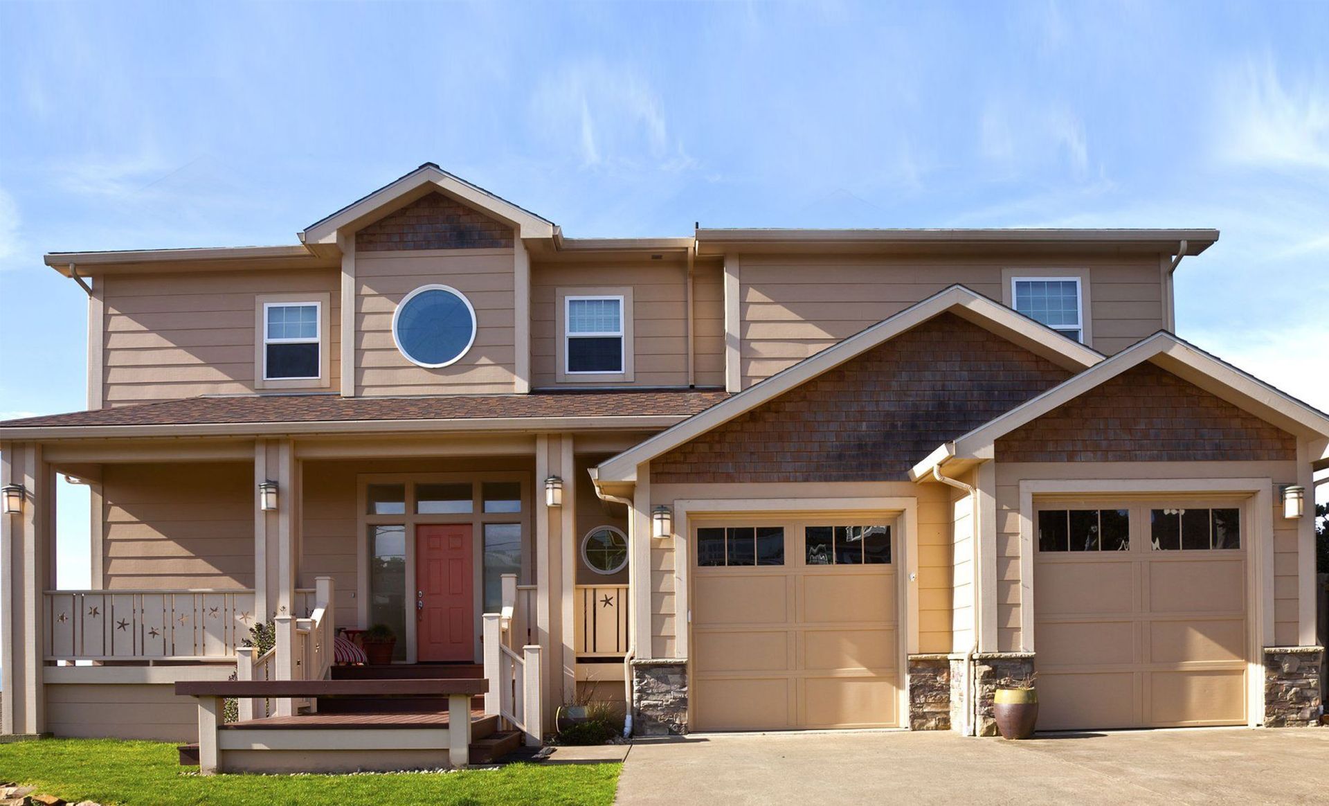 Two-story beige house with a porch and two-car garage under a blue sky.