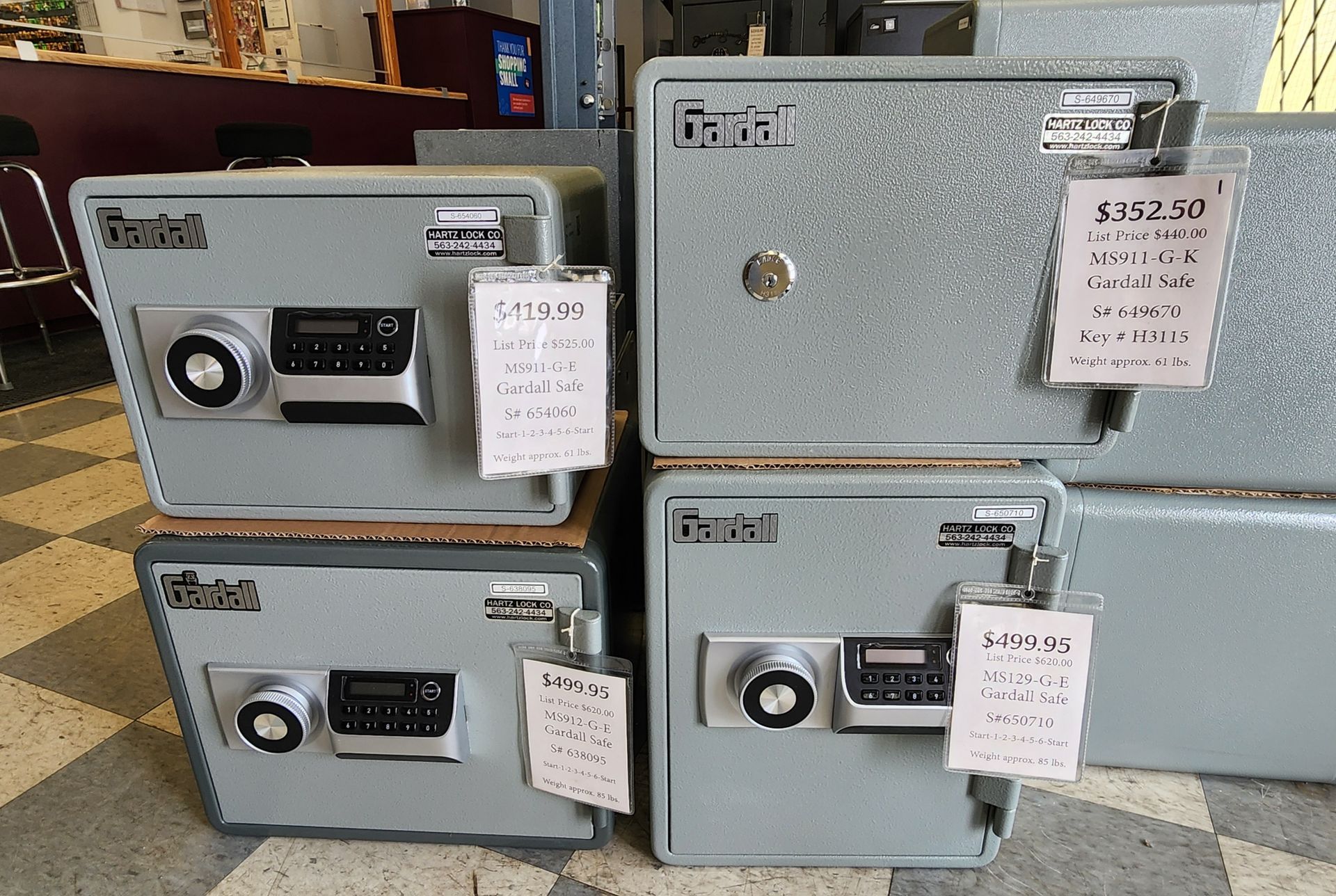 Four grey Fanta safes with digital keypads and tags are displayed on a tiled floor in a retail setting.