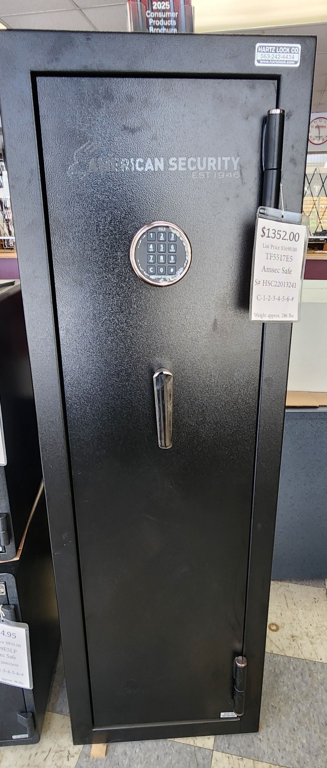 A tall, black, metal gun safe with an electronic keypad lock and a vertical handle, standing on a store floor.